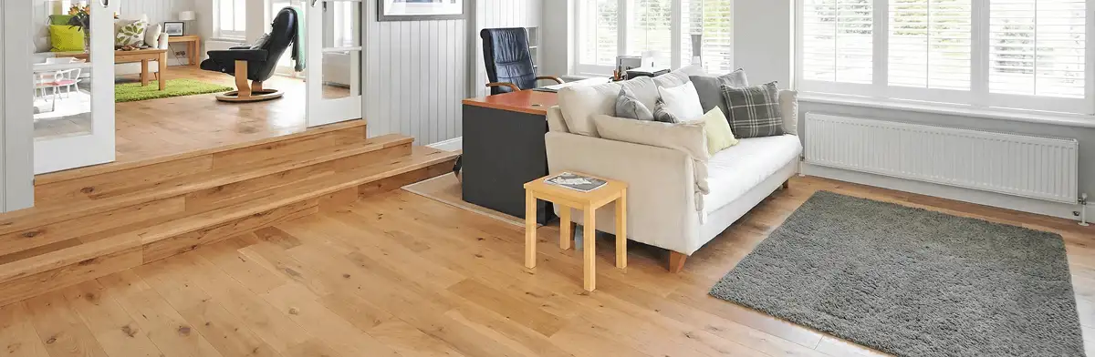 A modern living room with professionally installed laminate flooring, a beige sofa, a small side table, a gray rug, and large windows with white shutters in Tampa, FL